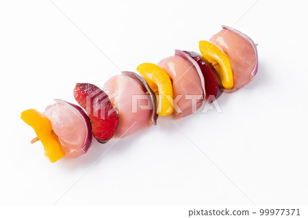 Raw chicken leg meat skewers with vegetables,plums,peppers,onions, on a white background.Uncooked mixed meat skewer with peppers.Skewers with pieces of raw meat, red, yellow and green pepper.Top view. 99977371