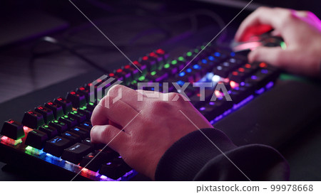 Male hands is typing on the computer keyboard, close up view. Man working on the pc computer. Human hands typing on the colourful gaming keyboard. Fingers typing on the led rgb keyboard. 99978668