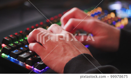 Male hands is typing on the computer keyboard, close up view. Man working on the pc computer. Human hands typing on the colourful gaming keyboard. Fingers typing on the led rgb keyboard. 99978675