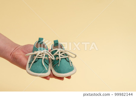 Children's shoes on a woman's palm. The idea of motherhood and the expectation of a newborn 99982144