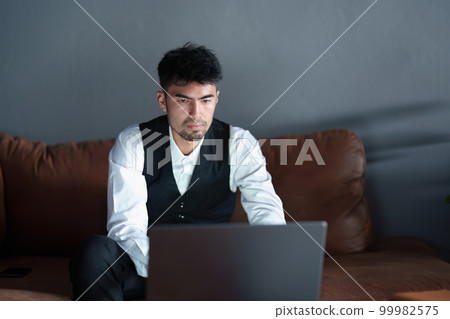 Portrait of a handsome, discreet Asian man sitting on the sofa using a computer. Portrait of a handsome, discreet Asian man sitting on the sofa using a computer. 99982575