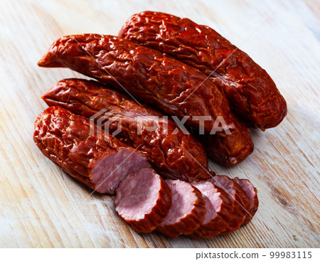Sliced half-smoked sausages susena on wooden table. Traditional Chezh meat products Sliced half-smoked sausages susena on wooden table. Traditional Chezh meat products 99983115