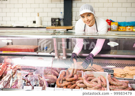 Young woman puts sausages in showcase 99983479