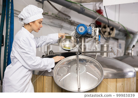 Female brewmaster pouring hop pellets from bowl into fermenter 99983839