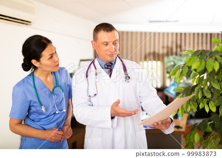 Experienced doctor advising female colleague about diagnosis of patient 99983873
