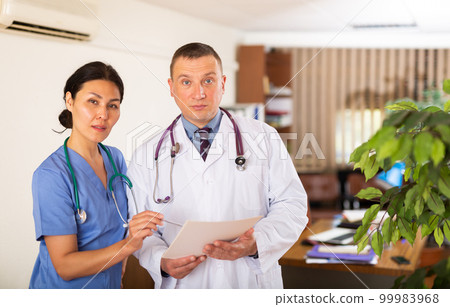 Two doctors checking patient papers in clinic 99983968