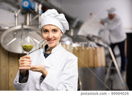 Portrait of a positive female brewer with a glass of hops at brewery 99984026
