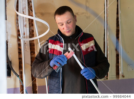 Plumber installs new plastic pipes in house under construction 99984044