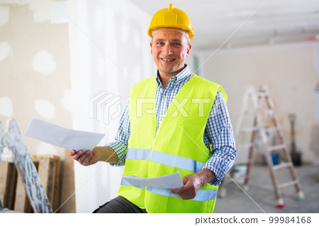 Man with documents in her hands stands in the middle of renovated room in cottage Man with documents in her hands stands in the middle of renovated room in cottage 99984168