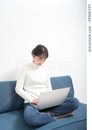 女人盤腿坐在沙發上，使用筆記本電腦 99986397