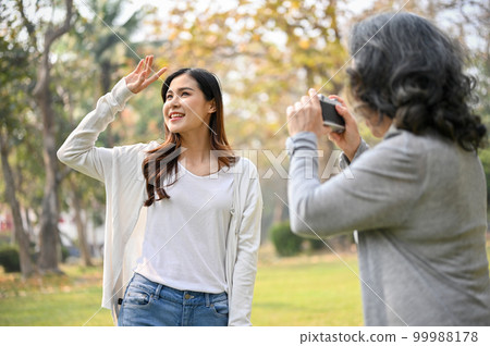 Happy Asian grandma taking a picture of her granddaughter while strolling in the park Happy Asian grandma taking a picture of her granddaughter while strolling in the park 99988178