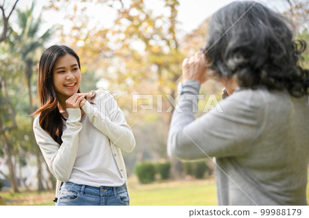 Happy Asian grandma taking a picture of her lovely granddaughter with a retro camera in the park 99988179