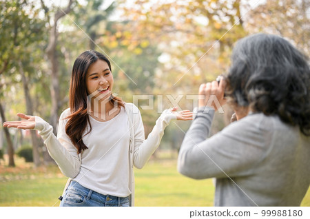Happy Asian grandmother taking a picture of her lovely granddaughter while strolling in the park Happy Asian grandmother taking a picture of her lovely granddaughter while strolling in the park 99988180