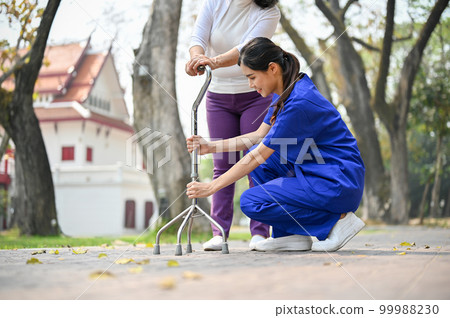 Caring and supportive female caregiver helping an old lady to walk with a walking stick 99988230