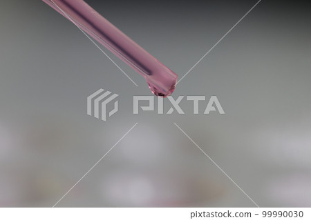 Glass pipette with purple liquid and drop on gray background. Glass pipette with purple liquid and drop on gray background. 99990030