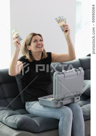 Excited woman with stacks of dollar banknotes in her hand and suitcase with money on her lap. Excited woman with stacks of dollar banknotes in her hand and suitcase with money on her lap. 99990064