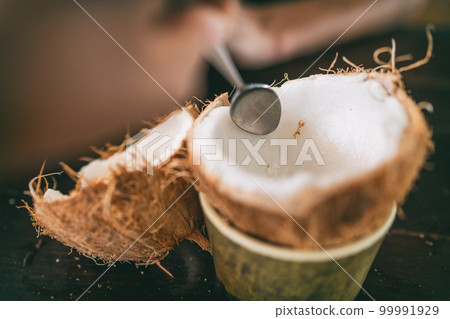 Fresh coconut being open and eaten in restaurant. Woman using spoon to remove meat from coco to eat fresh. Tropical food Fresh coconut being open and eaten in restaurant. Woman using spoon to remove meat from coco to eat fresh. Tropical food 99991929
