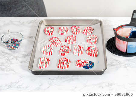 Flat lay. Dipping pretzels twists into melted chocolate to make red, white, and blue chocolate-covered pretzel twists. Flat lay. Dipping pretzels twists into melted chocolate to make red, white, and blue chocolate-covered pretzel twists. 99991960