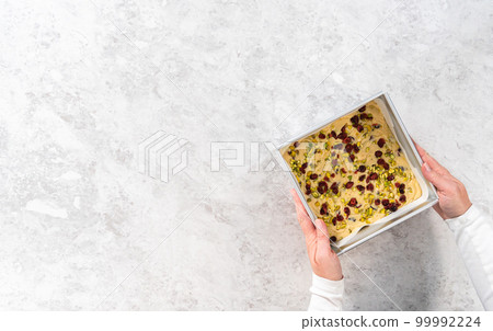 Flat lay. Filling square cheesecake pan lined with parchment paper with fudge mixture to prepare cranberry pistachio fudge. Flat lay. Filling square cheesecake pan lined with parchment paper with fudge mixture to prepare cranberry pistachio fudge. 99992224