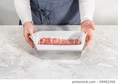 Preparing classic meatloaf in a loaf pan lined with parchment paper. 99992268