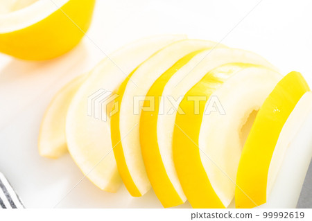 Slicong golden dewlicious melon on a white cutting board. Slicong golden dewlicious melon on a white cutting board. 99992619