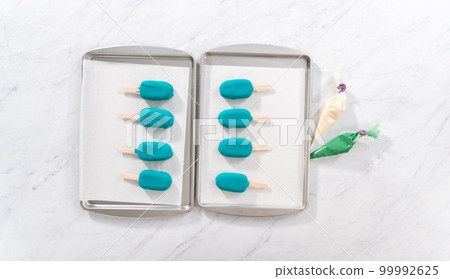 Flat lay. Decorating cakesicles with drizzled chocolate, chocolate mermaid tails, and seashells. 99992625