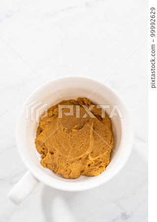 Pouring cake batter into the mug to prepare pumpkin mug cake. 99992629