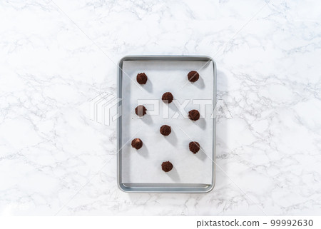 Flat lay. Scooping cookie dough with a small dough scoop into a baking sheet lined with parchment paper to bake peppermint white chocolate cookies. 99992630