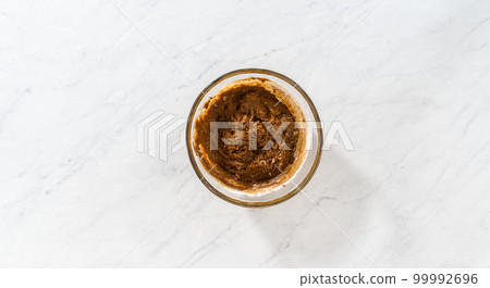Flat lay. Mixing wet and dry ingredients with a hand whisk in a glass mixing bowl to bake gingerbread bundt cake with caramel filling. Flat lay. Mixing wet and dry ingredients with a hand whisk in a glass mixing bowl to bake gingerbread bundt cake with caramel filling. 99992696