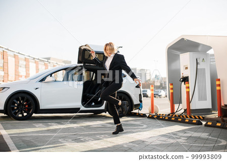 Woman dancing outdoors while car charging on station Woman dancing outdoors while car charging on station 99993809
