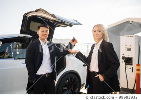 Sales agent giving keys from new electric car to woman Sales agent giving keys from new electric car to woman 99993932