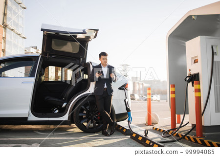 Man using mobile and credit card while charging electro car Man using mobile and credit card while charging electro car 99994085