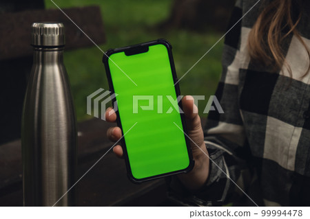 Mobile phone social media green screen Chroma key. Reusable steel thermo water bottle on wooden bench. Sustainable lifestyle. Plastic free zero waste free living. Go green Woman student work study 99994478