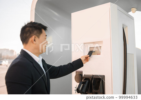 Asian man using credit card at EV charging station Asian man using credit card at EV charging station 99994633