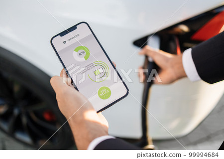 Close up of man charging electric car and using smartphone 99994684