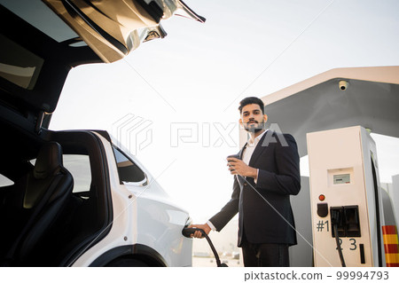 Indian man drinking coffee and charging electro auto Indian man drinking coffee and charging electro auto 99994793