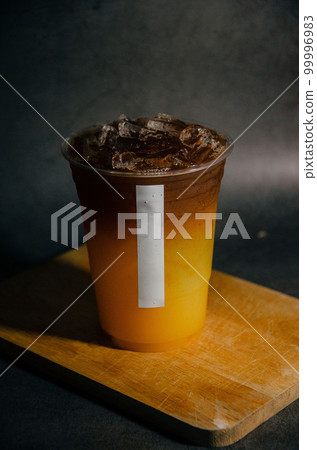 Close up of americano and orange juice in plastic glass with white sticker tag on wooden plate with gray background Close up of americano and orange juice in plastic glass with white sticker tag on wooden plate with gray background 99996983