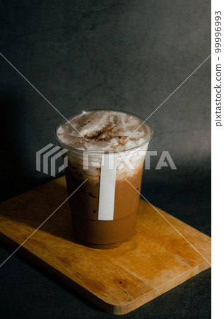 Close up of  iced mocha in plastic glass with white sticker tag on wooden plate with gray background 99996993