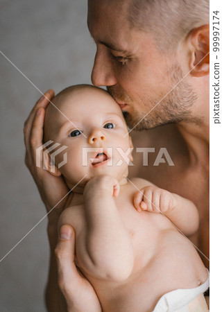 A young father holds his newborn son in a diaper in his arms and kisses him A young father holds his newborn son in a diaper in his arms and kisses him 99997174