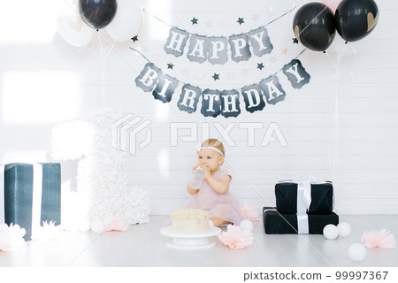 Birthday girl 1 year sitting in the photo zone surrounded by gifts, flowers 99997367