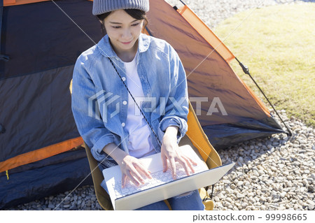A young woman using a laptop in front of a tent Workation image 99998665