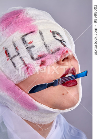 Bandaged head with blood stains after surgery. Young woman with scalpel in her teeth asking for help. Bandaged head with blood stains after surgery. Young woman with scalpel in her teeth asking for help. 99999002