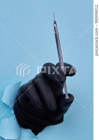 Hand holding gray cosmetic syringe on blue background. Black rubber latex glove. Hand holding gray cosmetic syringe on blue background. Black rubber latex glove. 99999012