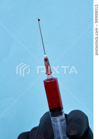 Close up syringe with blood on the needle. Vertical shot blue background. Close up syringe with blood on the needle. Vertical shot blue background. 99999013