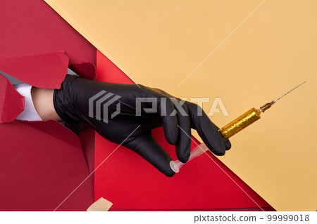 Close up hand holding syringe with yellow glitter. Red and yellow paper background. 99999018