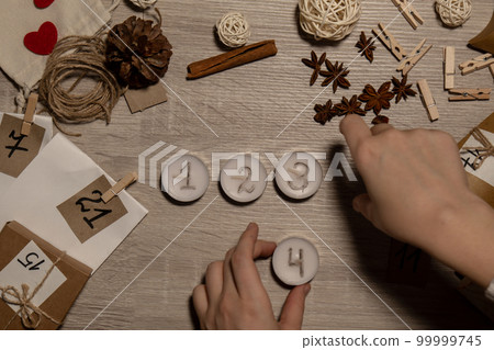 Unrecognizable young woman paint numbers on tea candles. Female making homemade advent calendar Made with your own hands step by step DIY crafts do it yourself. Preparation to christmas concept 99999745