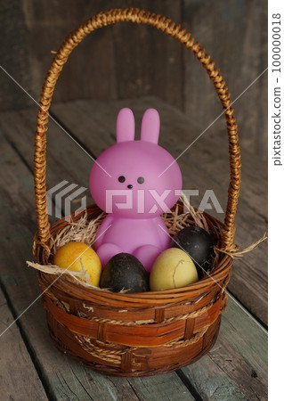 Bunny or rabbit and colorful Esther's eggs in the basket. Adorable small pink rabbit and Esther's eggs on wood background. Rabit standing 100000018