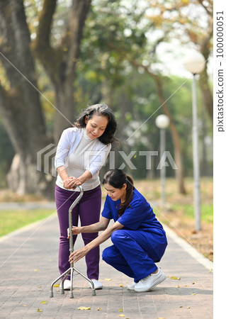 Attentive practitioner nurse assisting senior female walking with tripod cane. Assistance, rehabilitation and health 100000051