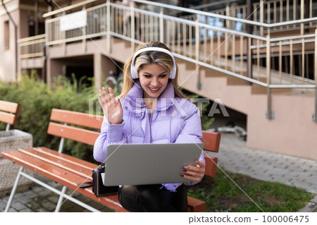 girl student during a break talking with a friend via video call in headphones on the street girl student during a break talking with a friend via video call in headphones on the street 100006475