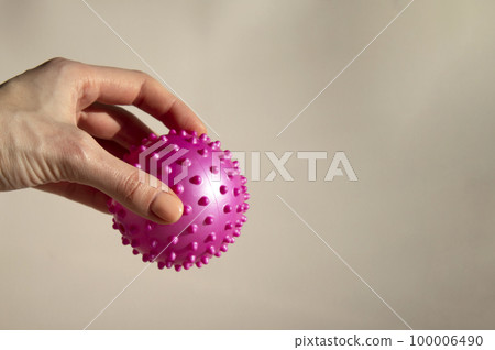 A woman is holding a pink ball with spikes. Myofascial release. Copy space, beige background. A woman is holding a pink ball with spikes. Myofascial release. Copy space, beige background. 100006490